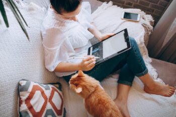 A women working at home with a cat next to her.